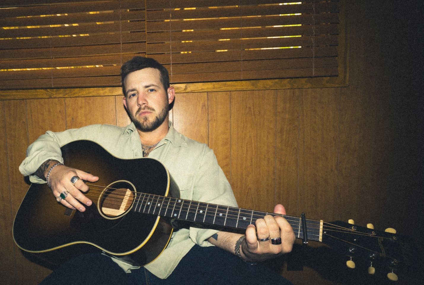 A man wearing a green shirt holding an acoustic guitar